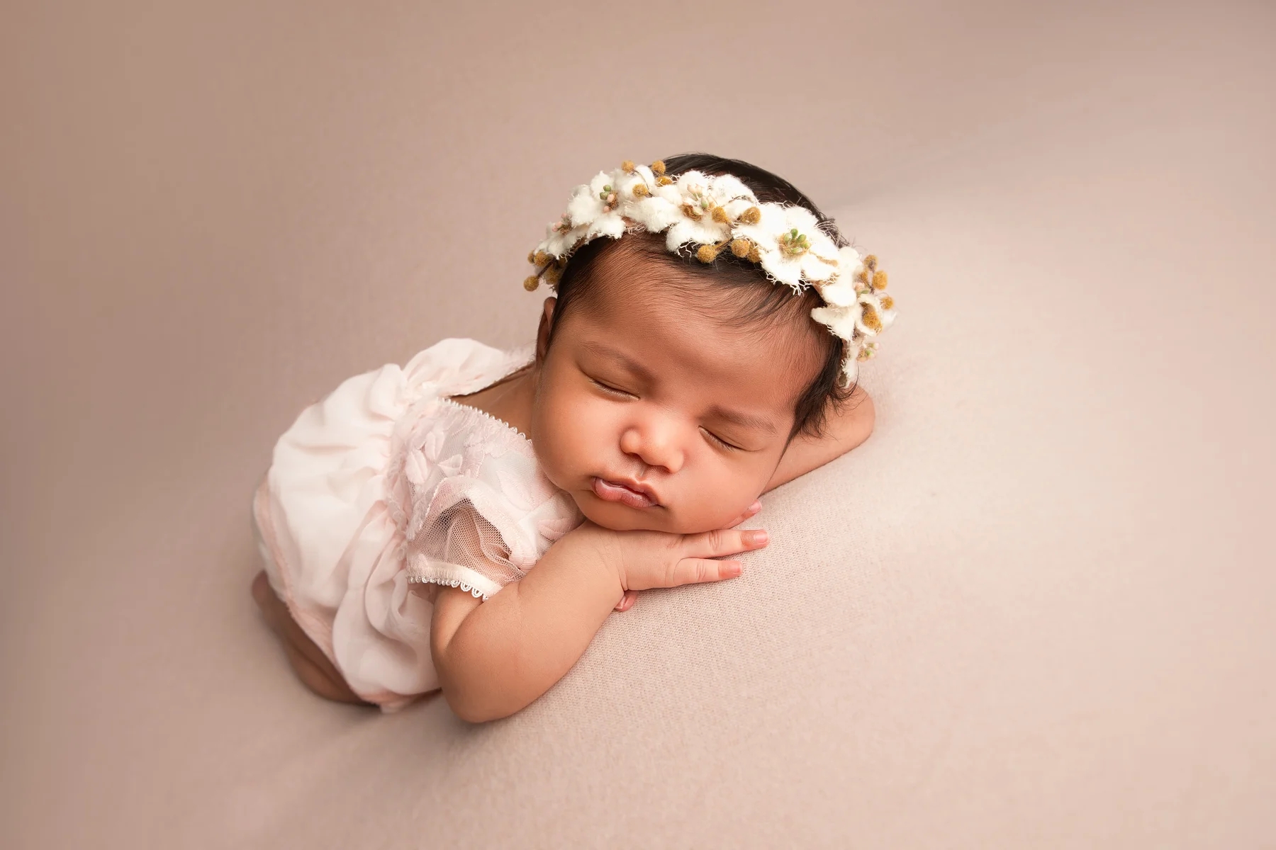 Newborn baby sleeping in a white outfit and floral headband in Ana Koska’s Timonium studio