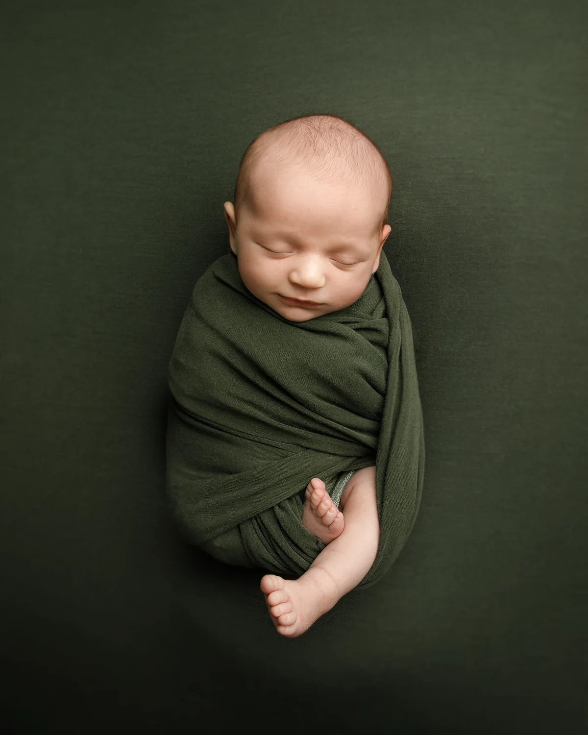 Sleeping newborn wrapped in deep green fabric during a studio portrait
