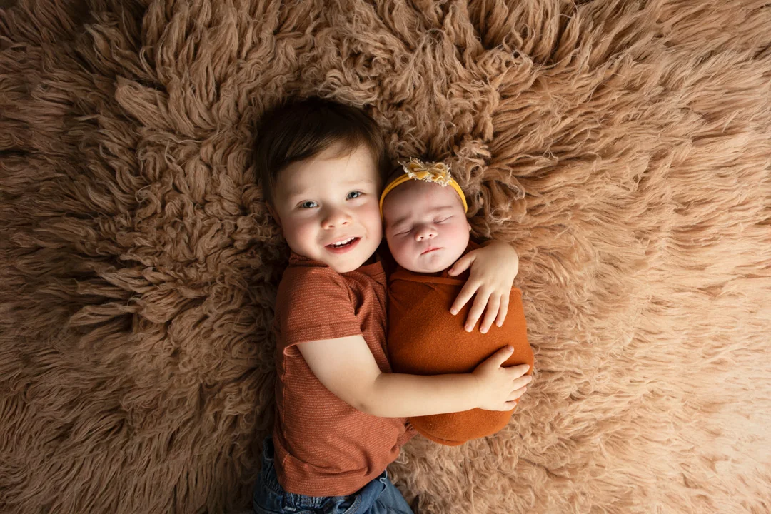 Young child hugging a sleeping newborn during a studio portrait