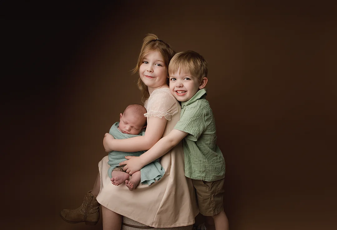 Two children holding a sleeping newborn during a studio portrait