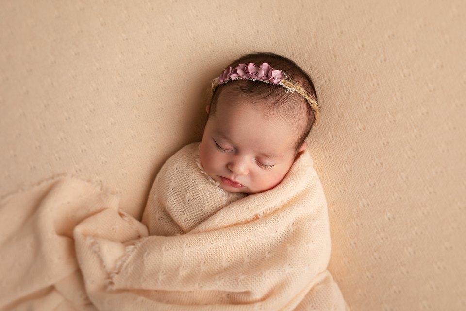 Sleeping newborn swaddled in cream with a pink floral headband