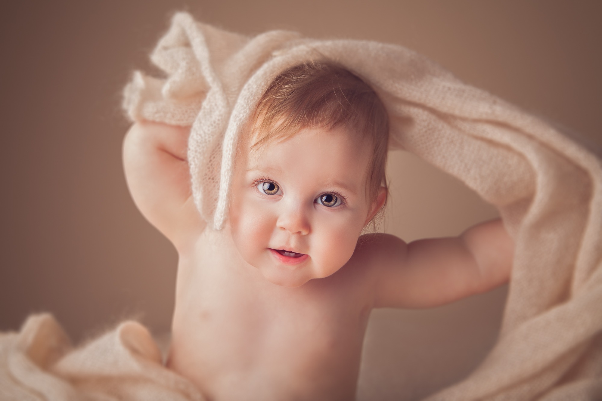 Baby smiling beneath a soft cream blanket during a milestone session