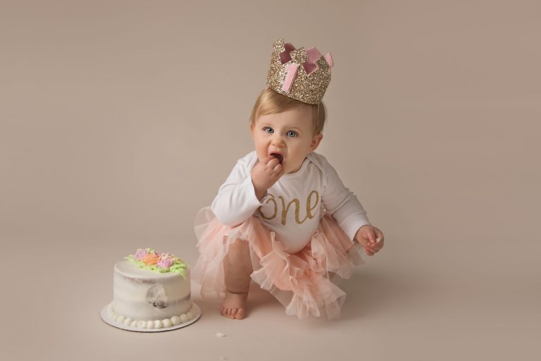 One-year-old girl wearing a birthday crown beside her cake during a milestone portrait session
