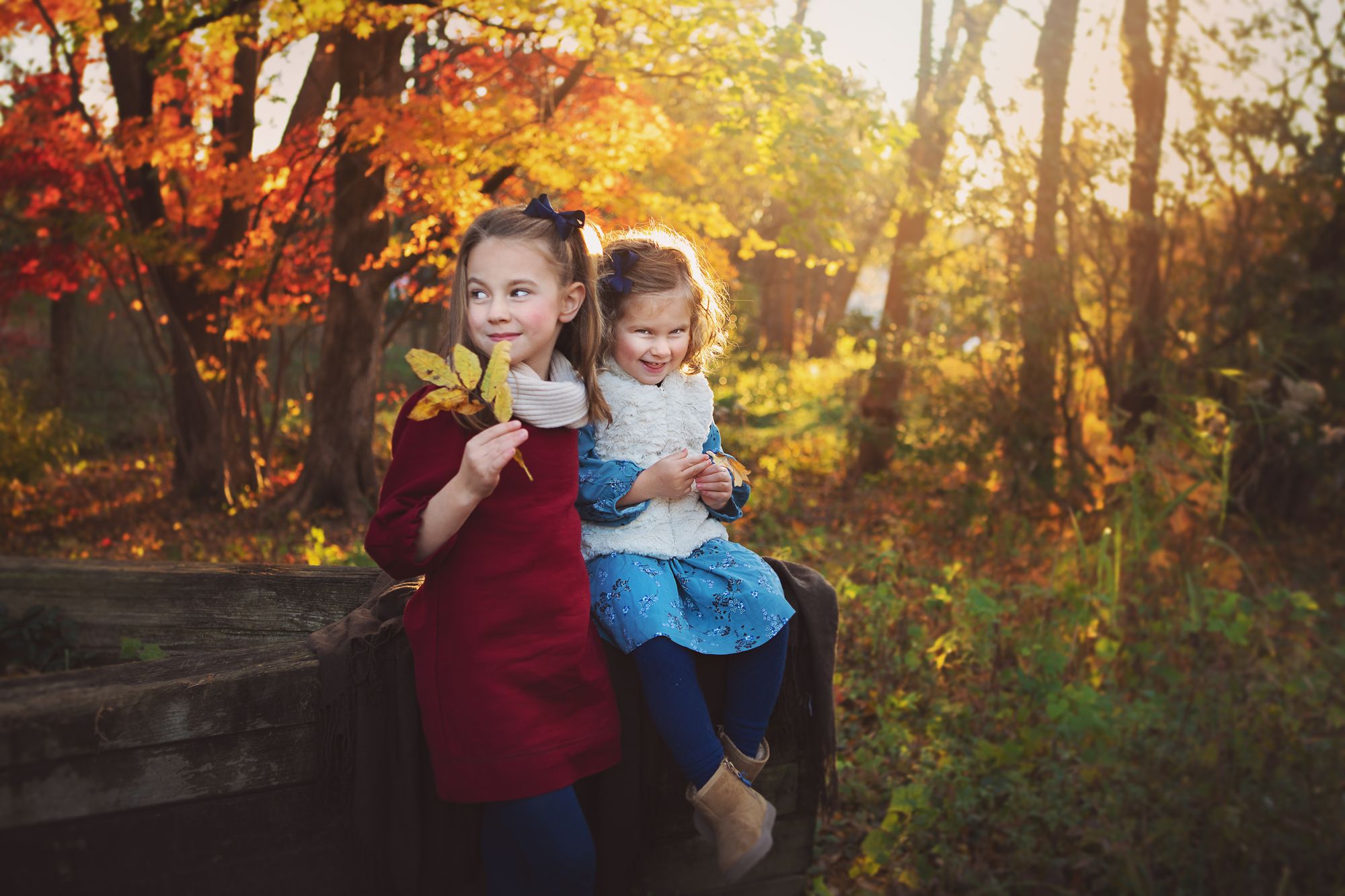 Two sisters sitting together among vivid autumn leaves during an outdoor portrait session