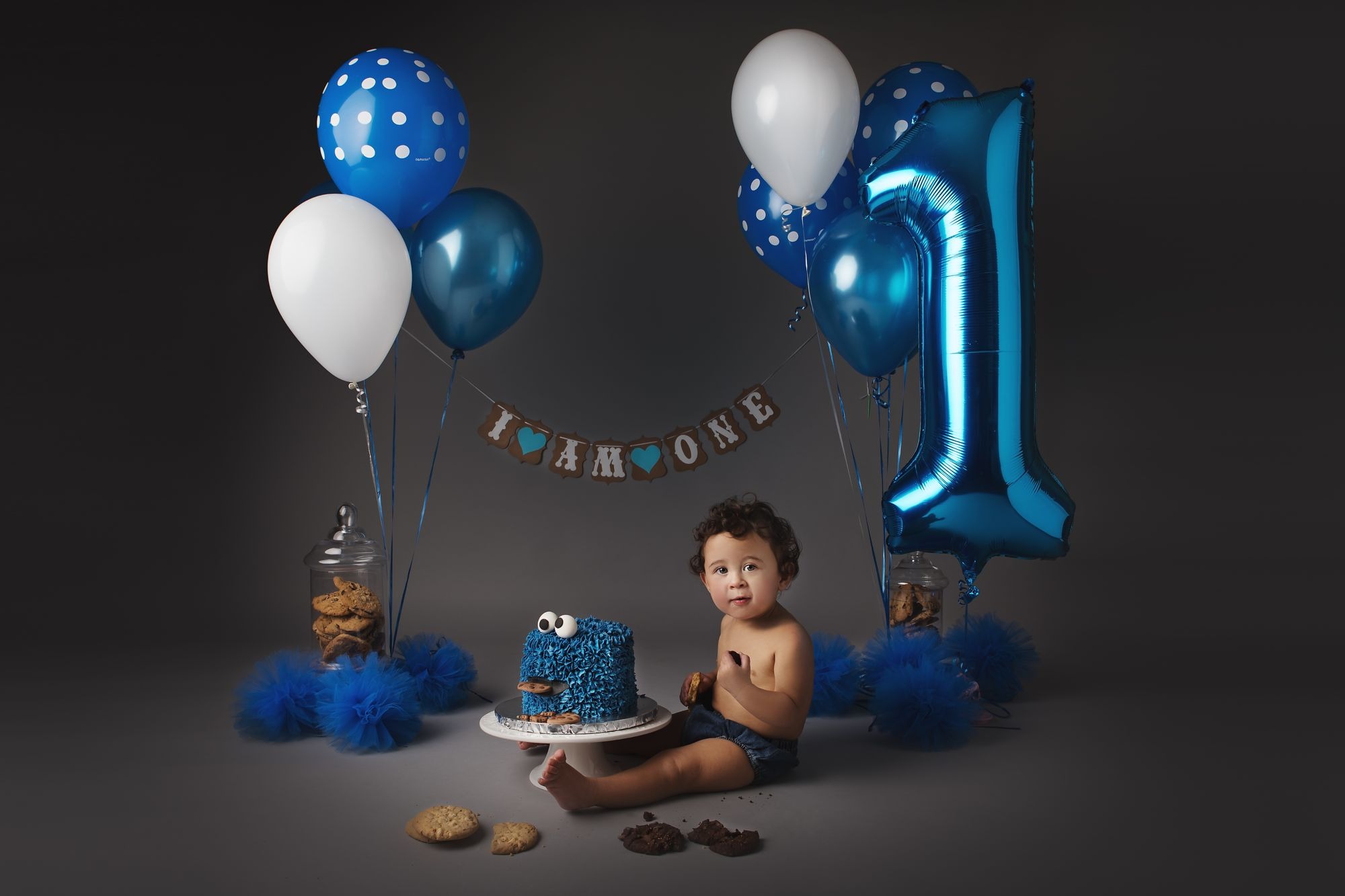 First birthday portrait with a blue balloon and cake setup