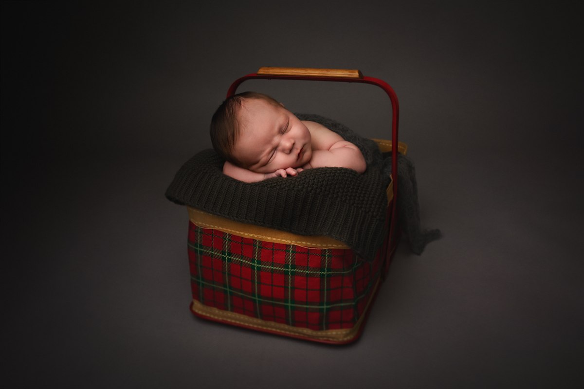 Sleeping newborn in a tartan holiday basket with a dark knit layer