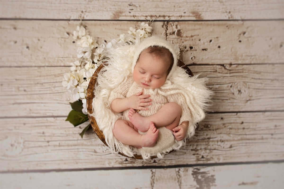 Sleeping newborn in a white floral basket on a rustic backdrop