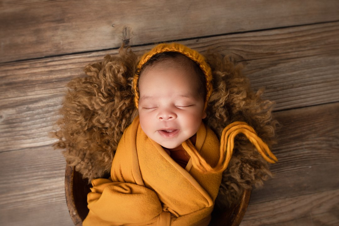Smiling newborn wrapped in mustard inside a padded round basket