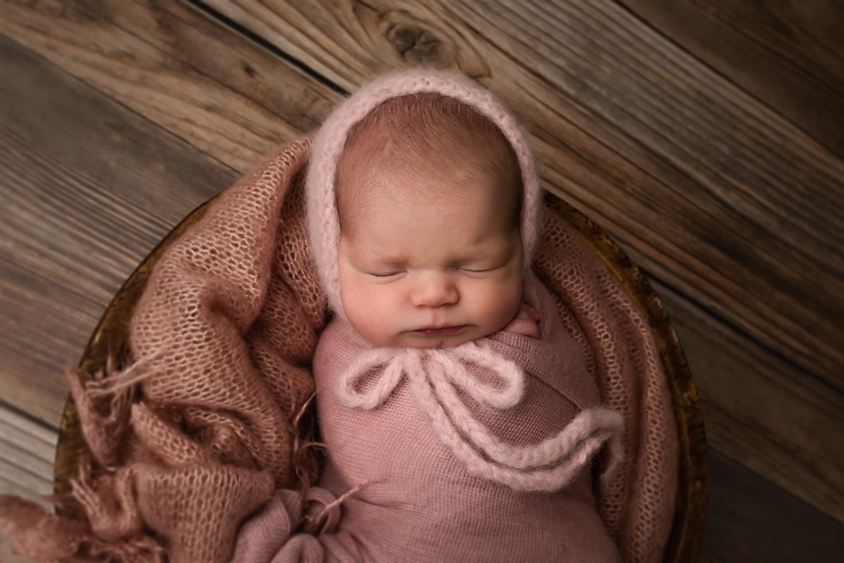 Wrapped newborn in a pink knit bonnet resting in a round basket