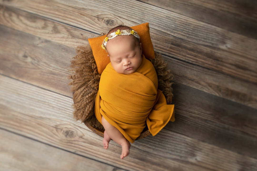 Overhead newborn portrait in a mustard wrap and shallow wooden basket