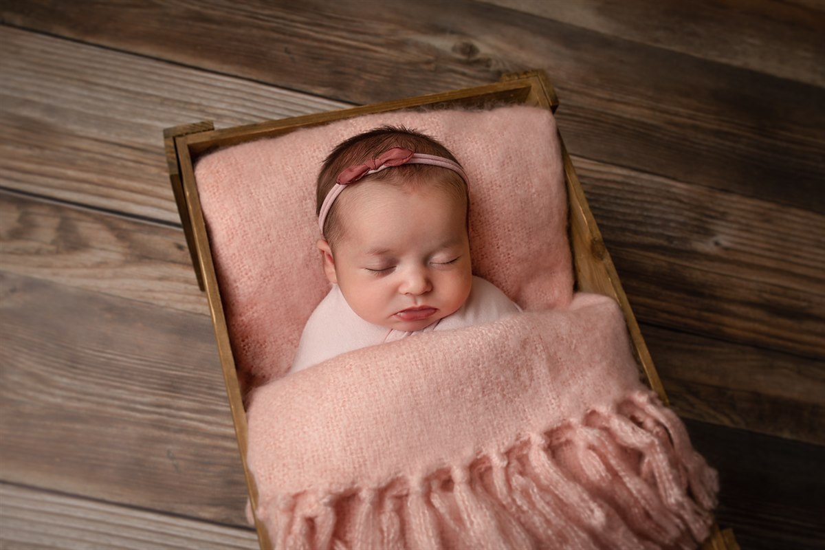 Sleeping newborn wrapped in blush inside a rectangular wooden crate