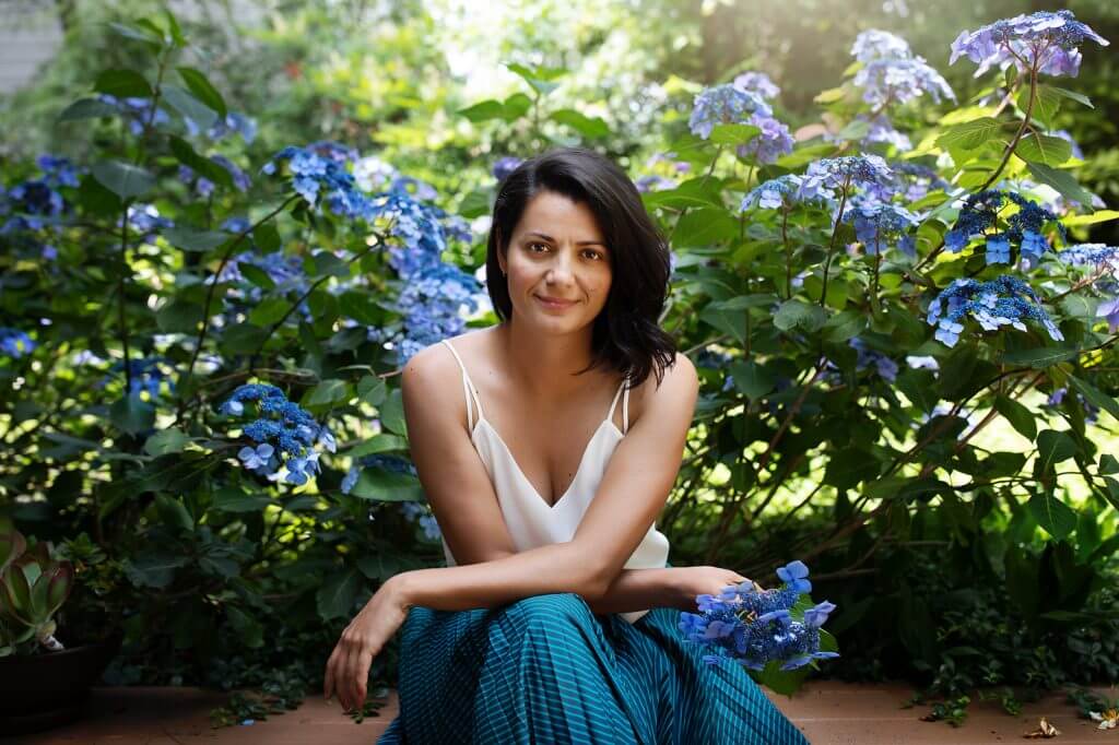 Portrait of photographer Ana Koska seated among blue hydrangeas