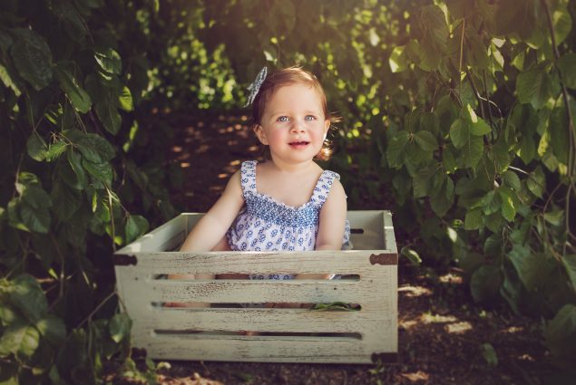 Baby girl in blue sitting in a crate