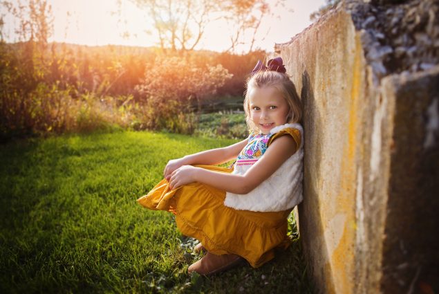Girl in yelow dress leaning on a wall