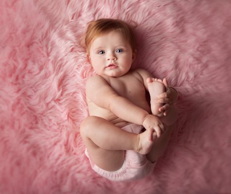 Baby playing with feet on pink blanket