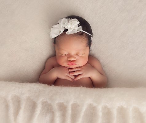 Newborn girl resting on a cream blanket with a delicate bow