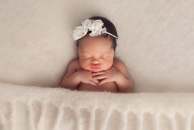 Newborn girl with white bow on her head covered with cream blanket