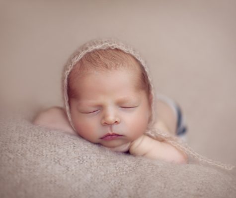 Newborn with a hat sleeping on beige blanket