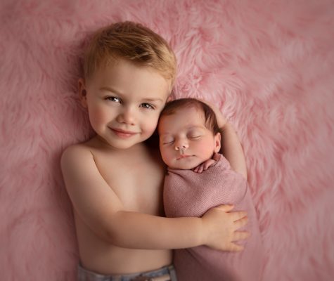 Older sibling gently hugging a swaddled newborn during a studio portrait