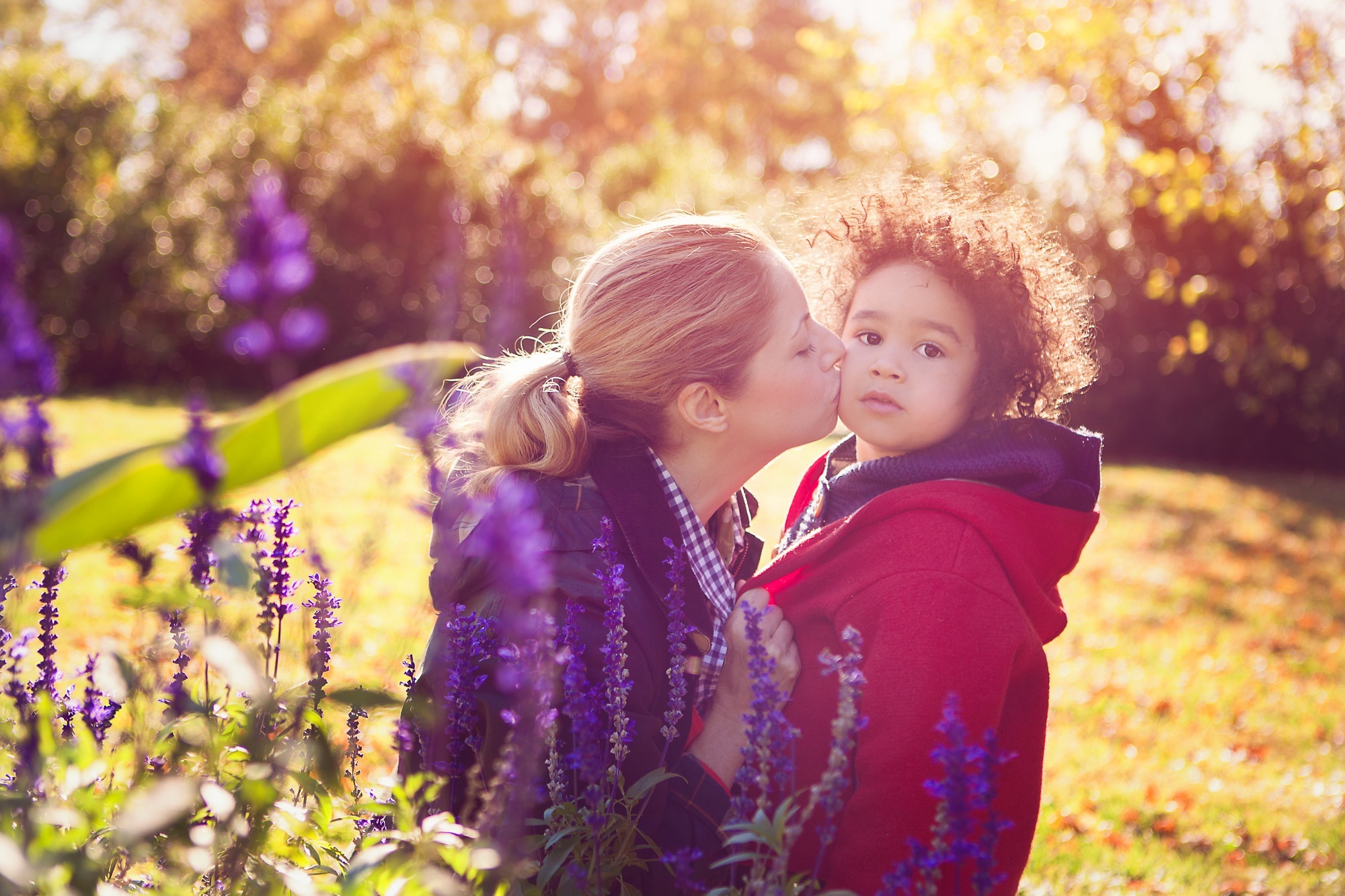 Portrait photo of a mother kissing her son in a garden 