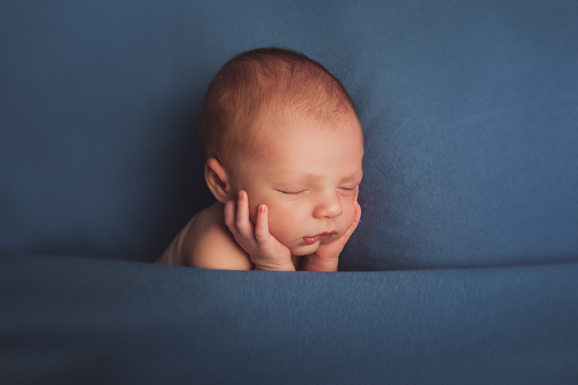 Portrait photo of a sleeping newborn under a blue blanket