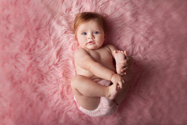 Baby playing with feet on pink blanket