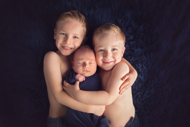 Brothers holding a baby on blue blanket