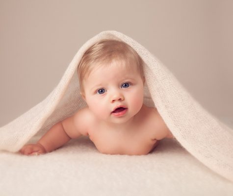 Child under a cream blanket in Milestone Photography Session