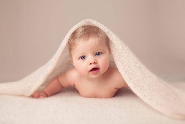 Child under a cream blanket in Milestone Photography Session