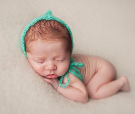 Newborn baby boy with green hat sleeping on beige blanket