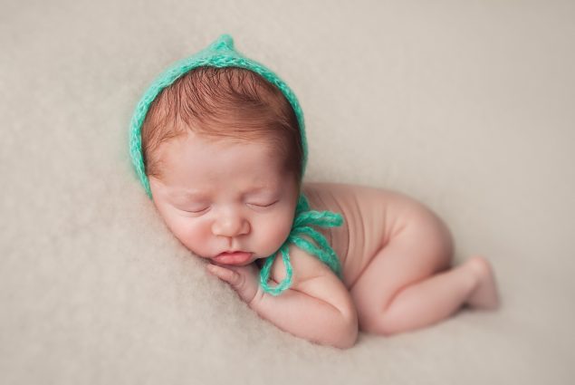 Newborn baby boy with green hat sleeping on beige blanket