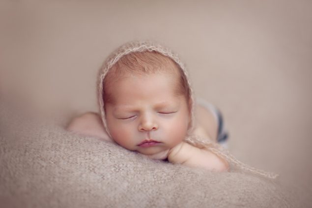 Newborn with a hat sleeping on beige blanket
