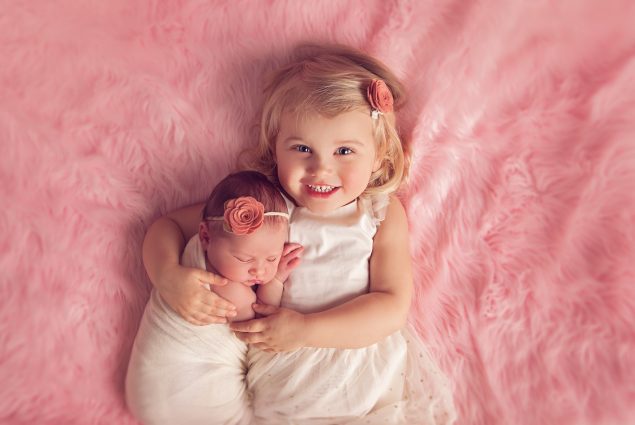 Portrait of a two-year-old with baby on pink blanket